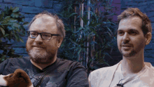a man with glasses and a beard holds a stuffed animal next to another man