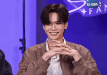a man in a brown jacket is smiling in front of a gmm fan sign