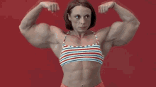 a very muscular woman in a striped top is flexing her muscles against a red background .