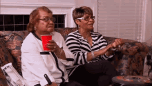 two women are sitting on a couch with a red cup