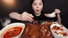 a woman is sitting at a table eating food with chopsticks and bowls of food