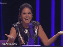 a woman in a sequined top speaking into a purple microphone with the hashtag @ lialmeida05
