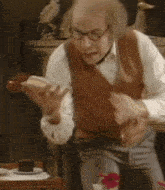 a man is sitting at a table eating a hot dog while wearing glasses .