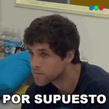 a man is sitting in front of a sign that says por supuesto on it