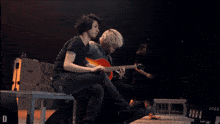 a man playing a guitar next to another man who is sitting on a bench