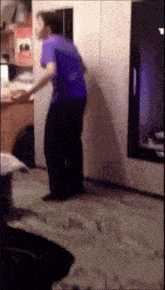 a man in a purple shirt is dancing in front of a tv