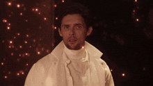 a man in a white coat and turtleneck is surrounded by lights
