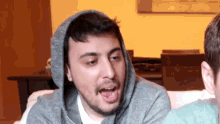 a man with a beard wearing a grey hoodie is sitting on a couch