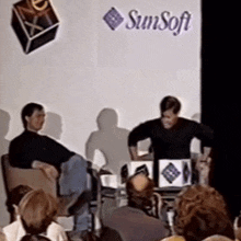 a group of people sit in front of a sunsoft sign