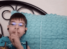 a young boy wearing glasses and ear buds is laying on a bed with his finger to his lips