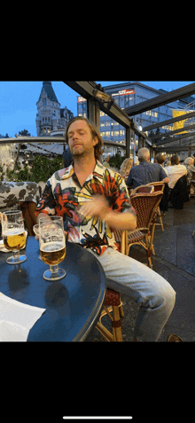a man in a colorful shirt sits at a table holding a glass of beer