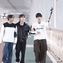 three young men are walking across a bridge one of them is wearing a umbro shirt