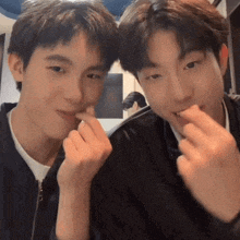 two young men are sitting next to each other and making a heart shape with their hands .