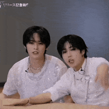 two young men are sitting at a table and one of them is wearing a microphone necklace