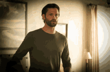 a man with a beard is standing in a room with a picture on the wall