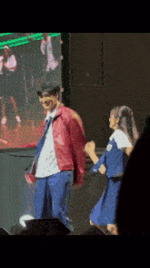 a man in a red jacket is dancing with a girl in a blue dress on a stage .