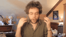 a man with glasses and a beard is making a funny face in front of a sign that says what the gif