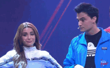 a man in a blue adidas jacket stands next to a woman in a white adidas jacket
