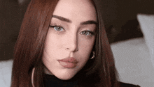 a close up of a woman 's face with long red hair and a black turtleneck .