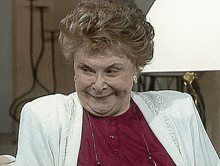 an older woman wearing a red shirt and a white jacket smiles