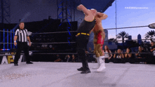 two men are wrestling in a ring with a referee standing behind them .