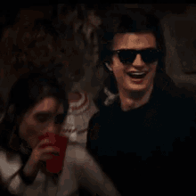 a man and a woman are sitting next to each other in a dark room . the woman is drinking from a red cup .