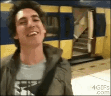 a man is smiling in front of a yellow and blue train with the website 4gifs.com in the corner