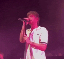 a man is singing into a microphone on a stage while wearing a white polo shirt .