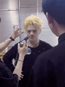 a man with blonde hair is being sprayed on his face by a man in a black shirt .