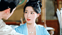a woman wearing a blue dress and a white necklace looks at a man