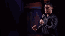 a man in a leather jacket is standing in front of a microphone on a stage .