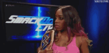 a woman in a pink tank top is holding a wwe championship belt .