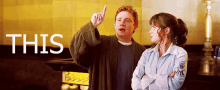 a man and a woman are standing next to each other and the man is pointing up while the woman looks at him .