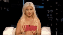 a woman with blonde hair is sitting in a chair with her hands on her knees .