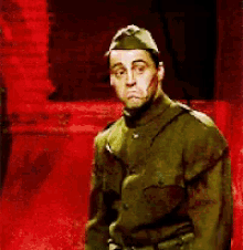 a man in a military uniform is standing in front of a red wall .