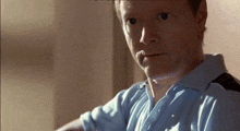 a man in a blue shirt looks at the camera with a cigarette in his mouth