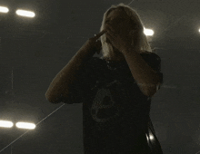 a woman wearing a black shirt with the letter a on it is singing into a microphone