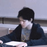 a young man wearing a hoodie and a t-shirt with the word vikings on it is sitting at a table .