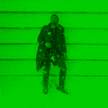 a man in a trench coat is standing in the snow in front of a green background .