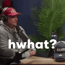 a man wearing headphones and a red hat is sitting in front of a microphone and says " what "