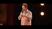 a man in a striped shirt is standing on a stage holding a microphone and dancing .