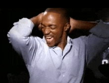 a man in a blue shirt is holding his head with his hands while laughing .