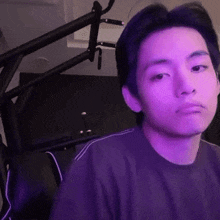 a young man in a purple shirt is sitting in front of a microphone in a room .