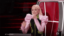 a woman in a pink and green jacket is sitting in a red chair with her hands in the air .
