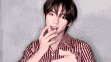 a young man in a red and white striped shirt is eating a piece of chocolate .