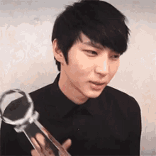 a young man in a black shirt is holding a trophy and making a funny face .