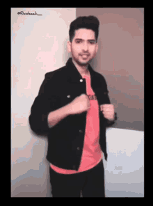 a man wearing a red shirt and a black jacket is standing in front of a wall ..
