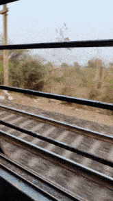 a train is going down the tracks with a fence in the foreground and trees in the background