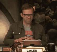 a man wearing glasses is sitting at a table with a tablet in his hand .
