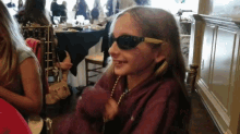 a young girl wearing sunglasses and a necklace is smiling